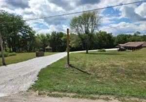 Curved gravel driveway leading past a gazebo and picnic area toward a rural home