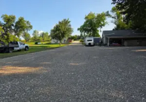 Wide gravel driveway and parking area beside a garage with an RV and pickup truck parked, on a rural property