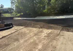 Construction site with white lime soil-stabilization material being spread over graded dirt, hoses and equipment in the foreground